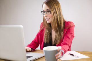 women with glasses on a laptop drinking coffee